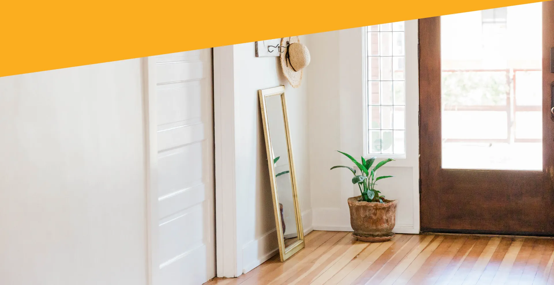 A bright hallway with a leaning mirror, a potted plant and a front door